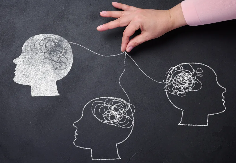 Drawing on a blackboard of three silhouettes of heads connected by threads. Visual representation of a psychologist in English and interconnection.