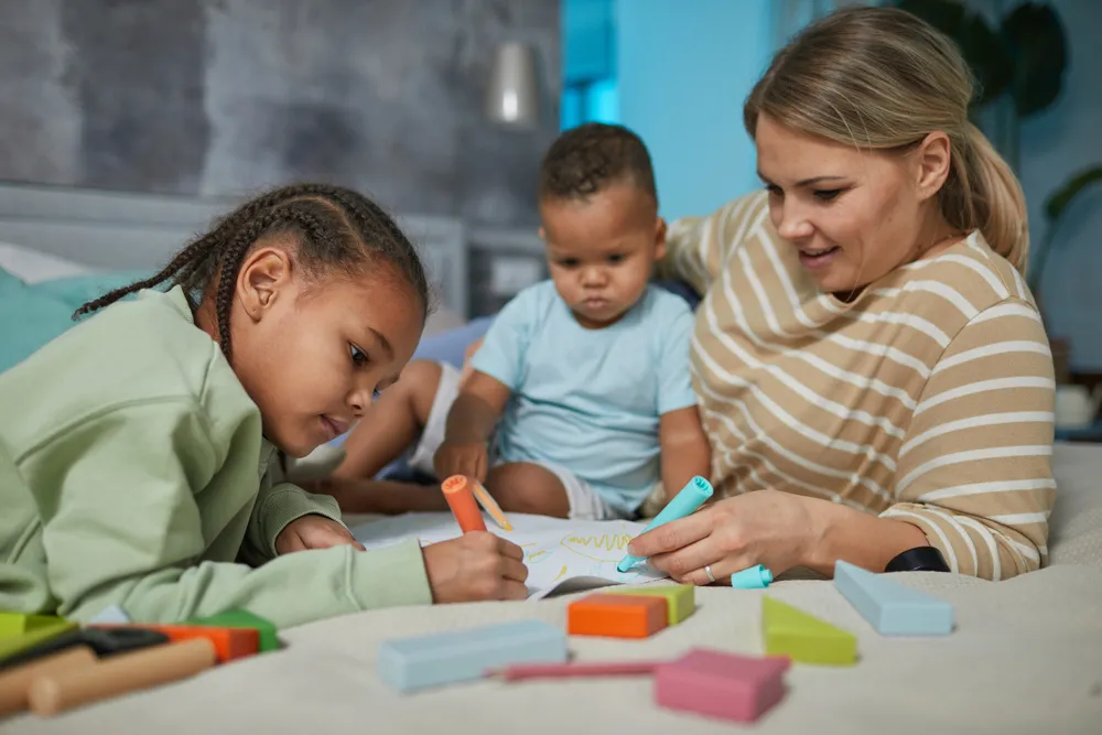 Mother and children drawing together in bed. Fostering positive parenting skills and strong family bonds.
