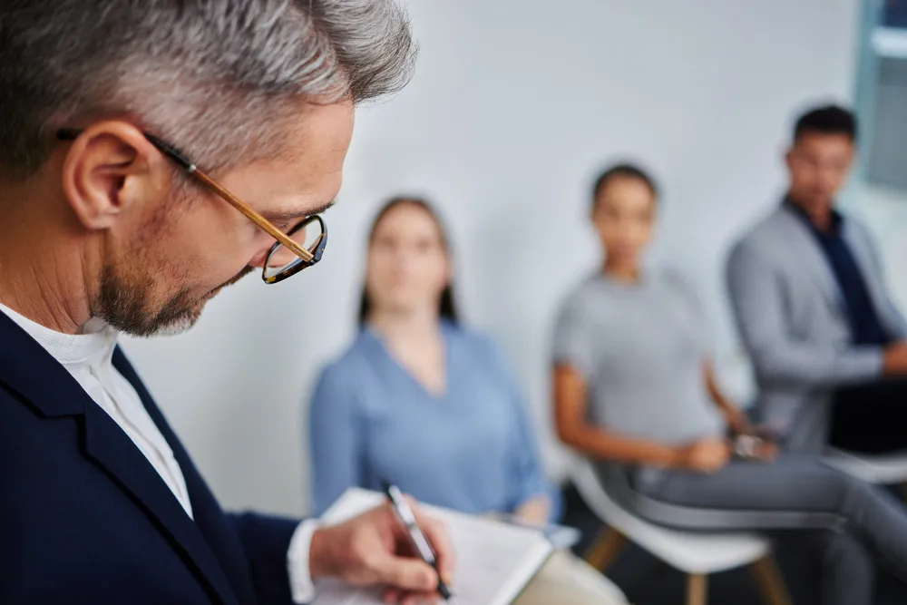 Close-up of a man writing notes in a notebook during a group session on anger management.