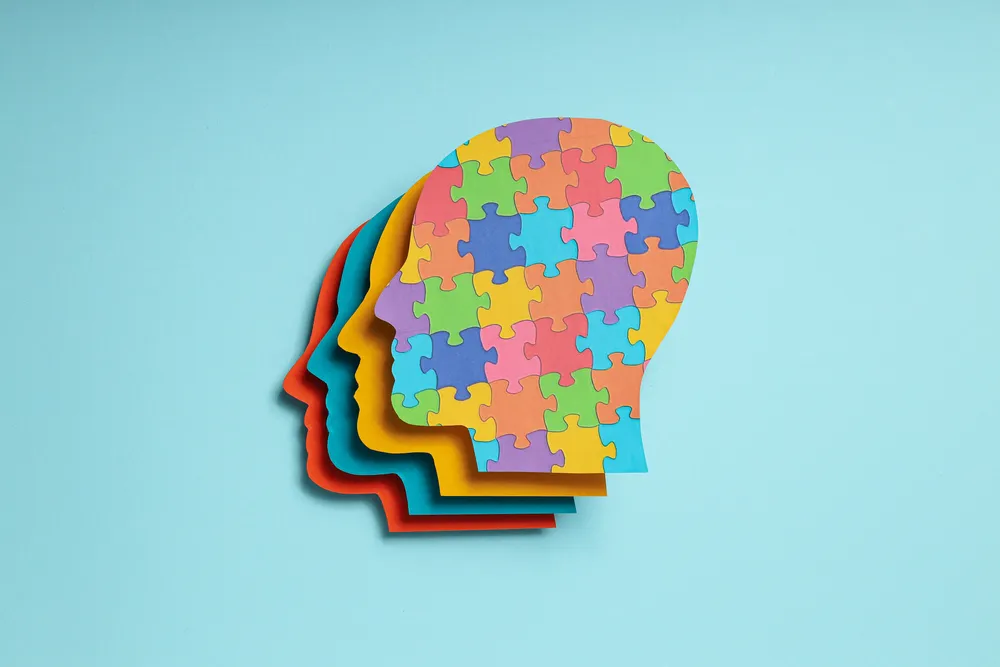 Cabezas humanas de papel de colores con textura de rompecabezas. Ilustra la mente humana y terapias de Psicología en línea.