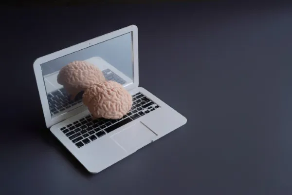 Modelo de cerebro sobre el teclado de una laptop blanca que representa el acceso a una terapia psicológica en línea.