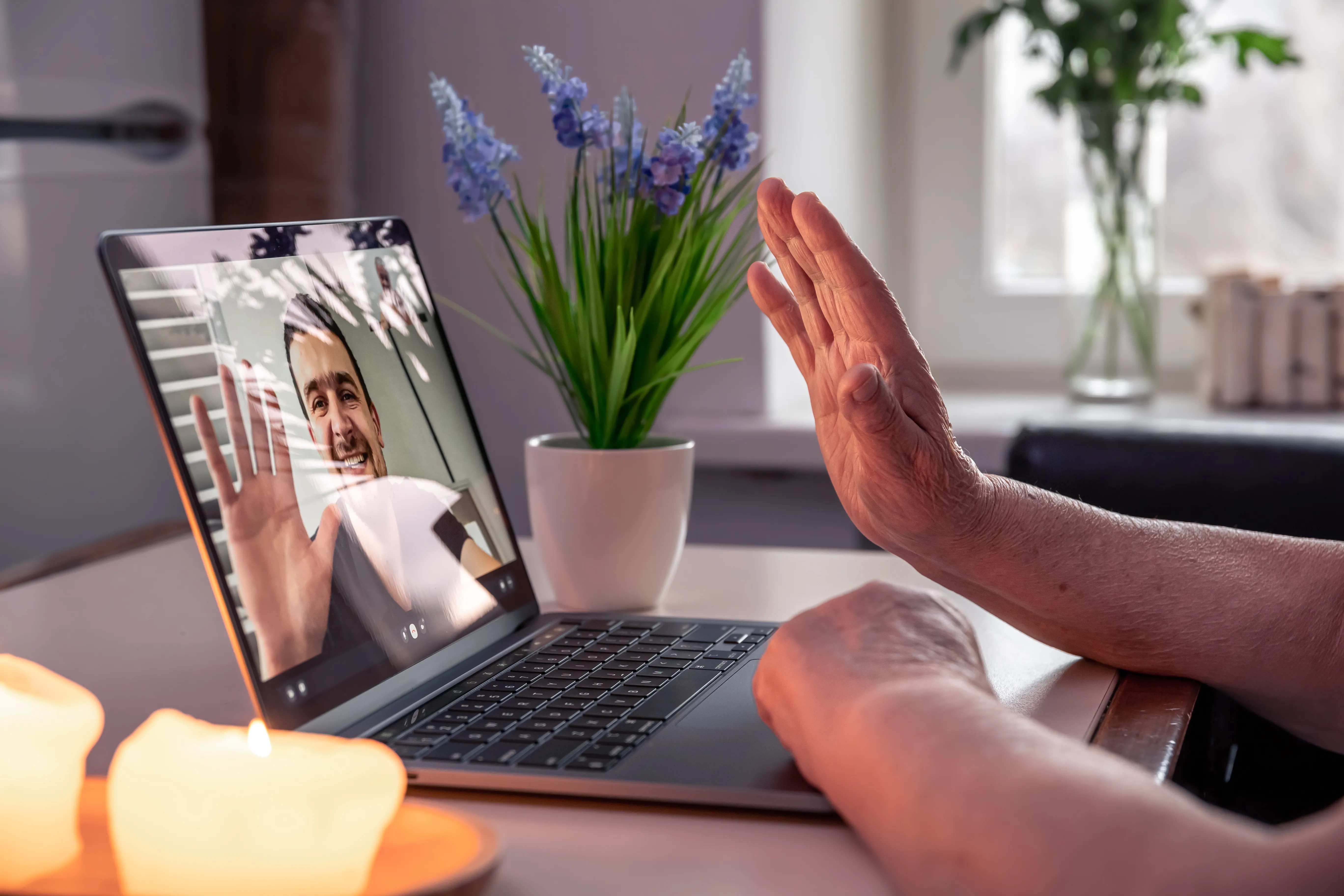 Manos de una anciana saludando a su hijo en una videollamada como parte de su terapia de estimulación cognitiva diaria.