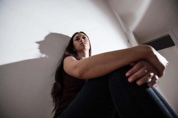 Young woman sitting on the floor with a distant look in her eyes, representing the isolation caused by anxiety disorders today.