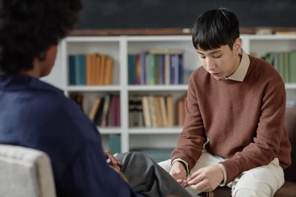 Chico joven en terapia para j&oacute;venes reflexionando mientras manipula un objeto durante una consulta con su terapeuta.