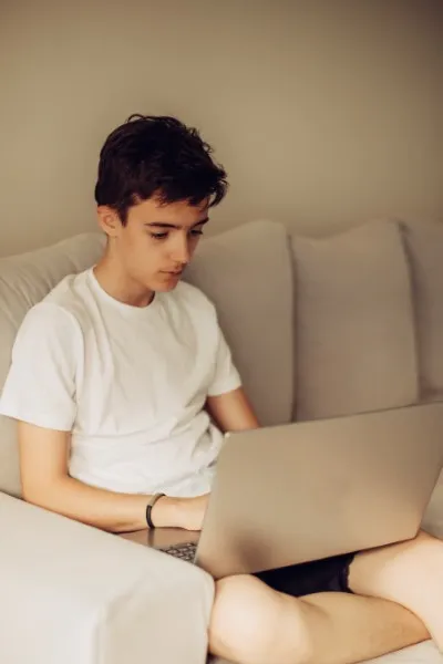 A young person sitting on a sofa using their laptop, an example of an online therapy for teenagers.
