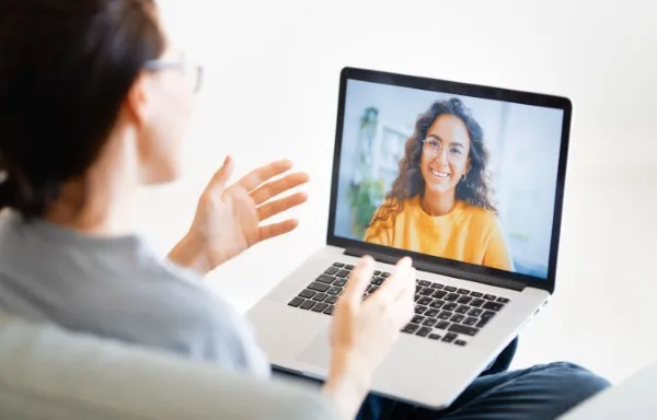 Una mujer joven platica con una especialista frente a su laptop durante una sesi&oacute;n de terapia para ansiedad desde casa.