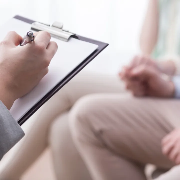 Especialista escribe un diagn&oacute;stico en su portapapeles durante una consulta de terapia para estr&eacute;s laboral.