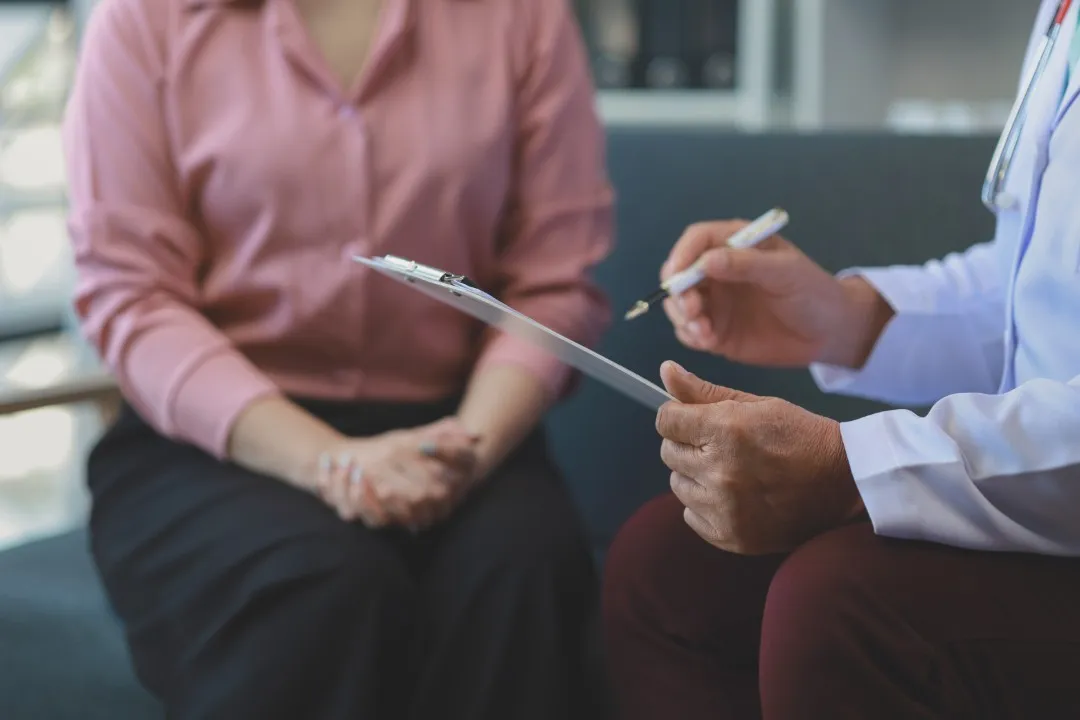 Especialista tomando notas durante una consulta presencial de terapia conductual mientras conversa con su paciente.