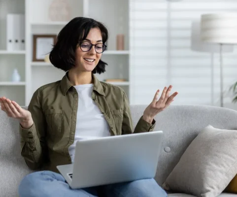 Mujer sonriente en su sof&aacute; hablando desde la computadora en su sesi&oacute;n de terapia individual online con su psic&oacute;loga.